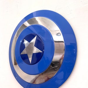 Puede incluir: Un escudo azul y plateado con un dise&ntilde;o de estrella plateada central. El escudo tiene forma circular con un anillo exterior azul, un anillo interior plateado y un centro azul. La estrella es de cinco puntas.