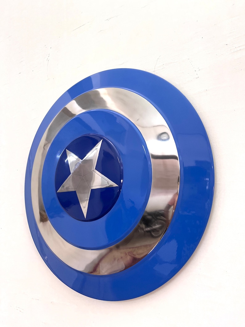 Puede incluir: Un escudo azul y plateado con un dise&ntilde;o de estrella plateada central. El escudo tiene forma circular con un anillo exterior azul, un anillo interior plateado y un centro azul. La estrella es de cinco puntas.