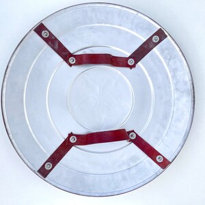 Pu&ograve; includere: Il retro di uno scudo rotondo in argento di Capitan America con cinturini in pelle rossa e rivetti metallici.
