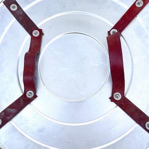 Pu&ograve; includere: Uno scudo di metallo argentato con una stella rossa al centro. Lo scudo ha due cinturini in pelle marrone con rivetti metallici fissati sul retro.