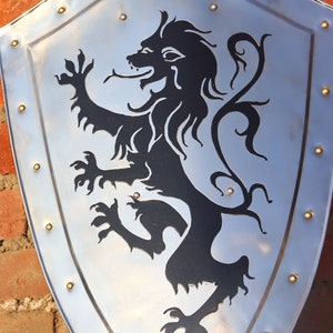 May include: A silver shield with a black lion design. The lion is standing on its hind legs with its tail curled up. The shield has a decorative border of gold studs.