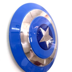 Puede incluir: Un escudo azul y plateado con un dise&ntilde;o de estrella plateada central. El escudo tiene un acabado brillante y una forma circular, con anillos conc&eacute;ntricos azules y plateados. Es un accesorio o art&iacute;culo de colecci&oacute;n.