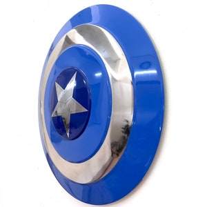 Puede incluir: Un escudo azul y plateado con un emblema de estrella. El escudo tiene un dise&ntilde;o circular con un anillo exterior azul, un anillo central plateado y un centro azul con una estrella plateada. El escudo es un accesorio.