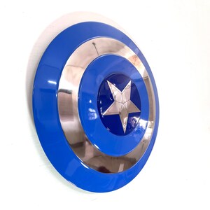 Puede incluir: Un escudo azul, plateado y blanco con una estrella en el centro. El escudo tiene un dise&ntilde;o circular con un anillo exterior azul, un anillo central plateado y un centro azul con una estrella plateada. El escudo es un accesorio o art&iacute;culo de colecci&oacute;n.