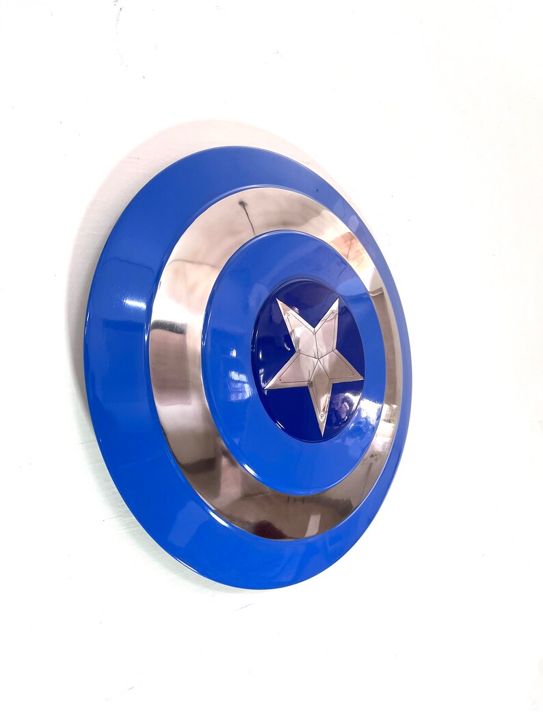 Puede incluir: Un escudo azul, plateado y blanco con una estrella en el centro. El escudo tiene un dise&ntilde;o circular con un anillo exterior azul, un anillo central plateado y un centro azul con una estrella plateada. El escudo es un accesorio o art&iacute;culo de colecci&oacute;n.