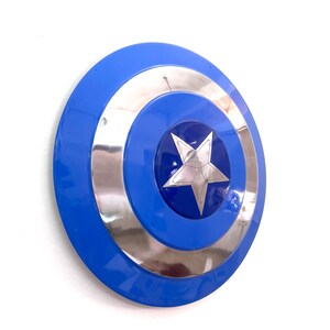 Puede incluir: Un escudo azul y plateado con una estrella de cinco puntas en el centro. El escudo tiene un acabado brillante y un dise&ntilde;o circular. Es un accesorio o art&iacute;culo de colecci&oacute;n.