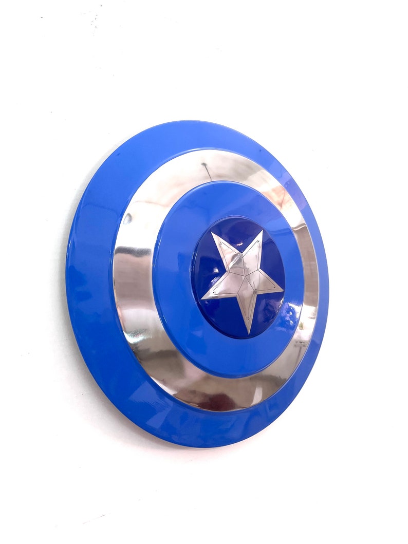 Puede incluir: Un escudo azul y plateado con una estrella de cinco puntas en el centro. El escudo tiene un acabado brillante y un dise&ntilde;o circular. Es un accesorio o art&iacute;culo de colecci&oacute;n.