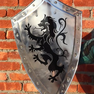 May include: A silver shield with a black lion design. The shield is decorated with metal rivets around the edge.