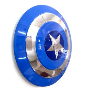 Puede incluir: Un escudo azul y plateado con una estrella plateada en el centro. El escudo tiene un dise&ntilde;o circular con anillos conc&eacute;ntricos azules y plateados. Es un accesorio o art&iacute;culo de colecci&oacute;n.