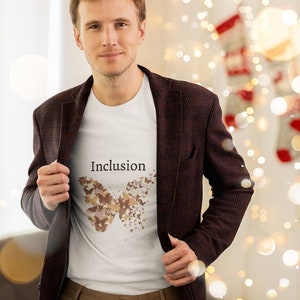 May include: A white t-shirt with a brown butterfly graphic and the word "Inclusion" printed on the front. The shirt is being worn by a person wearing a brown blazer and brown pants.