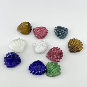 May include: Assortment of ten small, carved seashell-shaped pendants in various colors, including white, brown, green, blue, and pink.