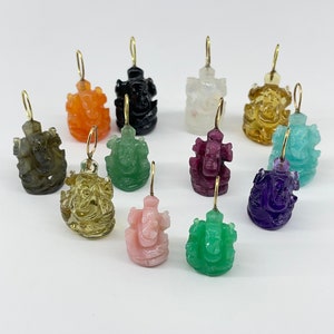 May include: Assortment of 12 small, intricately carved gemstone pendants featuring the Hindu deity Ganesha. Each pendant is a different color, including green, purple, pink, orange, and black.