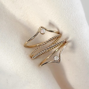 May include: Gold rings with a delicate design. The rings feature a twisted rope texture and small, round, white gemstones. The rings are arranged on a white fabric background, creating a simple and elegant aesthetic.