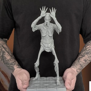 May include: A gray, 3D-printed statue of a creature with long fingers and a skeletal appearance. The statue is held in front of a black t-shirt with the same creature design. The image includes the text "HEADHUNTER" and "STL FILE PRINTED STL STATIC/ASSEMBLY".