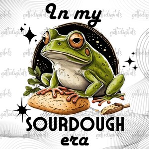 May include: A digital illustration features a green frog with orange eyes, perched on a loaf of sourdough bread. The text "In my SOURDOUGH era" is above and below the frog, with star accents.