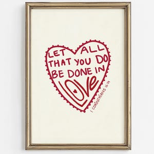 May include: Framed art print with a red heart design and the words "LET ALL THAT YOU DO BE DONE IN LOVE". The text is from 1 Corinthians 16:14. The print is in a gold-coloured frame.