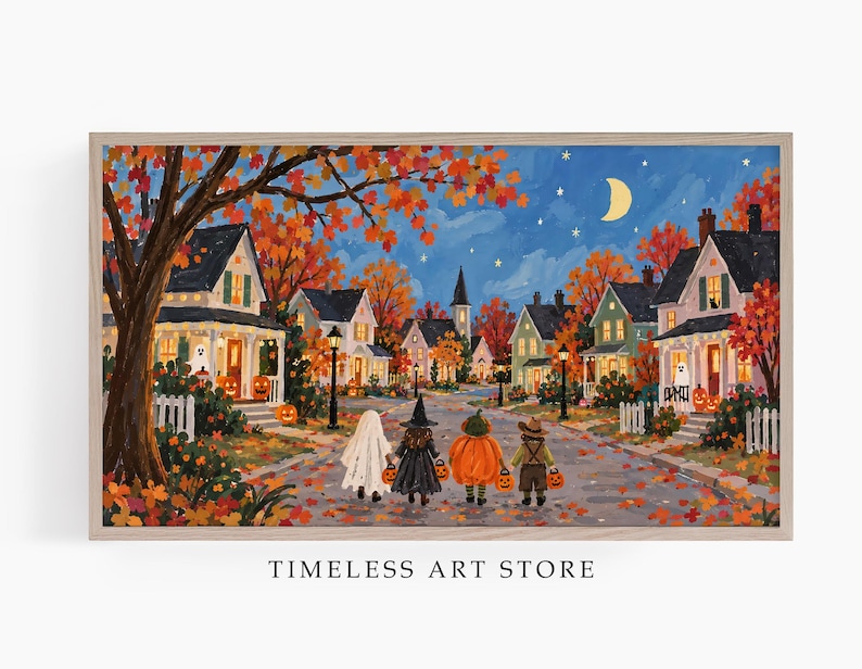 May include: A rectangular framed art print depicting a neighborhood street scene at night during autumn. Four figures in Halloween costumes walk down a leaf-covered road past houses with glowing windows, jack-o'-lanterns, and a crescent moon.