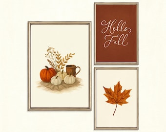 May include: Three framed wall art prints with metallic frames. One print shows a pumpkin, white gourds, dried foliage, and a mug. Another print has a dark orange background with the white text Hello Fall. The third print features a single maple leaf.
