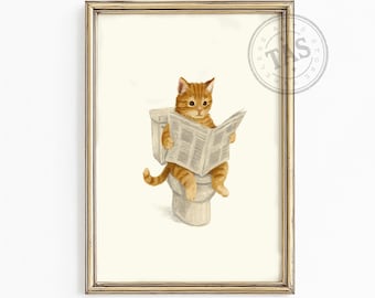 Op de afbeelding: Een ingelijste kunstdruk met een illustratie van een oranje cyperse kat die op een wit toilet zit en een krant leest. Het kunstwerk zit in een dunne, goudkleurige metalen lijst en bevat een cirkelvormig logo met de tekst TAS.