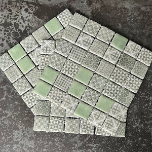 Könnte beinhalten: Eine Fliese aus grünem und grauem, gemustertem Keramikmosaik. Die Fliesen sind kleine Quadrate mit verschiedenen geometrischen Mustern.