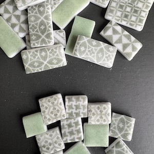 Könnte beinhalten: Eine Ansammlung kleiner, rechteckiger Fliesen in Grün- und Weißtönen. Einige Fliesen weisen geometrische Muster auf, andere sind einfarbig grün. Die Fliesen sind auf einer dunklen Oberfläche verstreut und zeigen ihre verschiedenen Designs und Farben.
