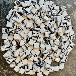 Puede incluir: Una colección de pequeños azulejos de cerámica blanca con diseños abstractos negros. Los azulejos están dispuestos en un patrón aleatorio.
