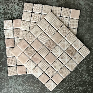 Op de afbeelding: Drie beige keramische tegelplaten met een geometrisch patroon. Elke plaat bestaat uit kleine vierkante tegels met verschillende ontwerpen, waaronder bloem- en geometrische motieven. De tegels zijn in een verspringend patroon gerangschikt.