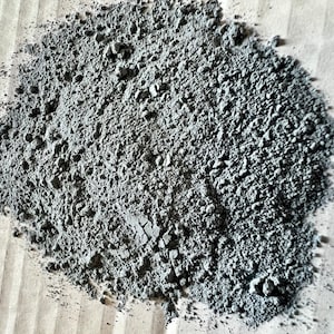 May include: A close-up of a pile of gray powder. The powder is fine and has a slightly rough texture.
