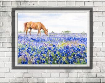May include: Watercolor painting of a brown horse grazing in a field of bluebonnets. The artwork is framed and set against a white brick wall. The sky is a light blue, and the flowers are a vibrant blue and purple.