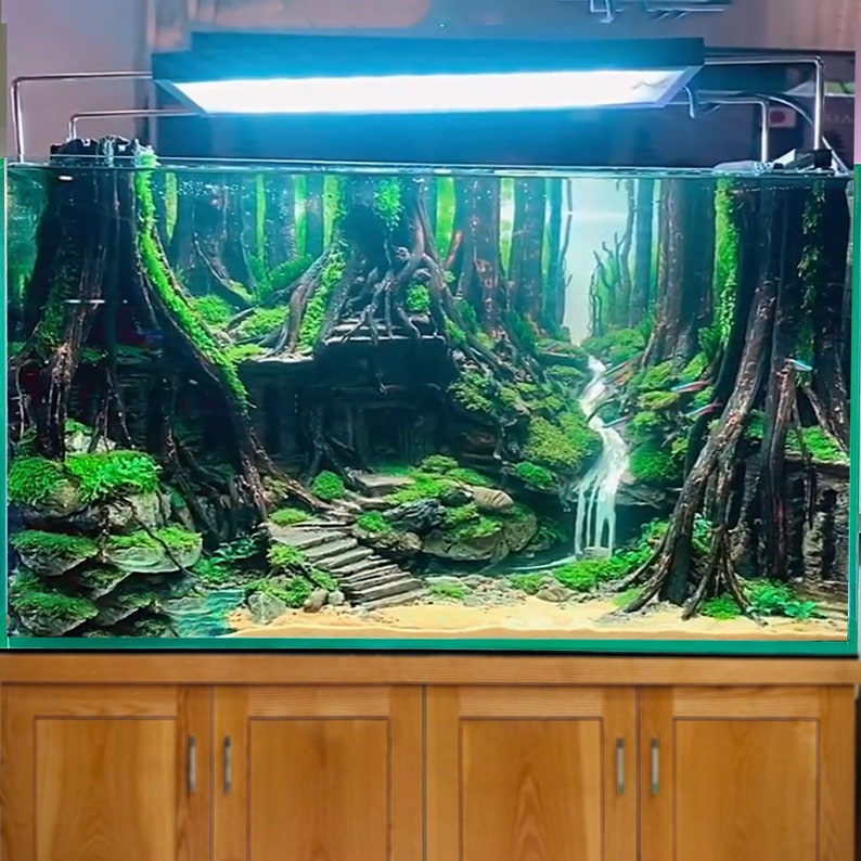 Puede incluir: Un acuario exuberante, verde, plantado con una cascada, rocas y una escena de bosque en miniatura. El acuario est&aacute; colocado sobre un gabinete de madera con dos puertas.