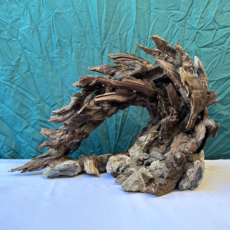 May include: A large, weathered piece of driftwood, shaped like a wave, with a base of smaller rocks. The driftwood is brown and gray, with a natural, rustic look.