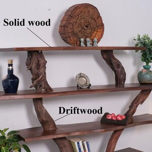 May include: A three-tiered shelf unit made of solid wood with driftwood branches as supports. The top shelf has a large, round, wooden slice with three small figurines on top. The middle shelf has a small, silver dish and a bottle of liquor. The bottom shelf has a small basket of red apples and a stack of books.