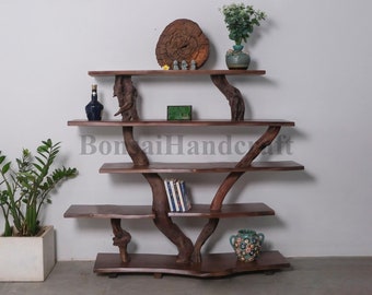 May include: A wooden shelf unit with a unique tree branch design. The shelves are made of dark brown wood and the branches are natural in color. The shelf unit has five shelves and is decorated with a small wooden circle, a green box, a blue bottle, a green vase with a plant, and a blue and white patterned vase.