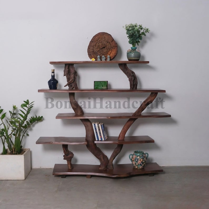 May include: A wooden shelf unit with a unique tree branch design. The shelves are made of dark brown wood and the branches are natural in color. The shelf unit has five shelves and is decorated with a small wooden circle, a green box, a blue bottle, a green vase with a plant, and a blue and white patterned vase.