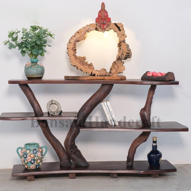 May include: A three-tiered wooden shelf unit with a unique, natural branch design. The shelves are made of dark wood and have a rustic, handcrafted look. The shelf unit is decorated with a small vase of flowers, a decorative plate, and a small statue of a person sitting on a wooden circle.