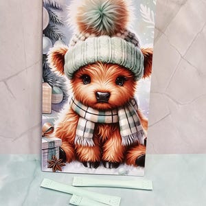 Può includere: Un biglietto di auguri con la scritta "Holy Cow" raffigura una mucca delle Highlands dei cartoni animati con cappello e sciarpa invernali. Sono presenti anche diversi pacchetti verde chiaro e un piccolo gruppo di abbellimenti rotondi e trasparenti.