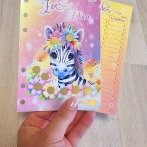 Op de afbeelding: Een roze en gele zebra stickerkaart met een kleurrijke zebra die een bloemenkrans draagt. De kaart heeft een sectie voor het registreren van punten en een sectie voor het registreren van het totaal. De kaart zegt "Zoe Zebra" bovenaan.