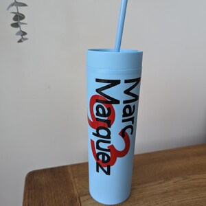 May include: A light blue tumbler with a black and red logo that says "Marc Marquez" and a clear plastic straw.