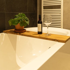 Peut inclure: Une baignoire blanche avec un plateau en bois sur le dessus. Le plateau contient une bouteille de vin et un verre à vin. Il y a également une plante en pot sur le plateau.