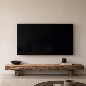 May include: A large rectangular black television screen mounted on a wall above a long, low-profile wooden bench. The bench is constructed from a thick, weathered timber beam with a natural wood grain texture and is supported by two block legs.
