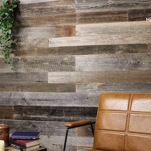 Könnte beinhalten: Rustikale Holzpaneelwand mit verschiedenen Braun-, Grau- und Beigetönen. Im Vordergrund ein brauner Ledersessel mit schwarzen Metallarmen. Ein kleiner Tisch mit Büchern, einer Kerze und einem Kupferbehälter. Hängende grüne Pflanze.