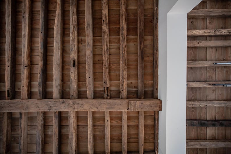 May include: A close-up view of a wooden ceiling with exposed beams. The ceiling is constructed of vertical and horizontal wooden beams, creating a grid-like pattern. The wood has a natural, aged appearance with varying shades of brown.