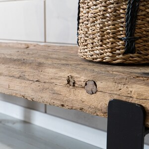 Puede incluir: Un estante de madera r&uacute;stica con una superficie desgastada y texturizada que presenta nudos y vetas naturales. El estante est&aacute; sostenido por un soporte de metal negro liso y sostiene una cesta de pasto marino tejida con detalles de cuerda negra.