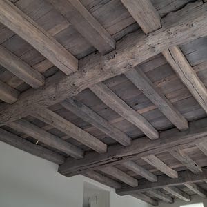 May include: A rustic wooden ceiling with exposed beams and planks. The wood has a weathered, gray-brown color, suggesting age and natural wear. The design features a grid-like pattern of beams and planks, creating a textured, architectural element.