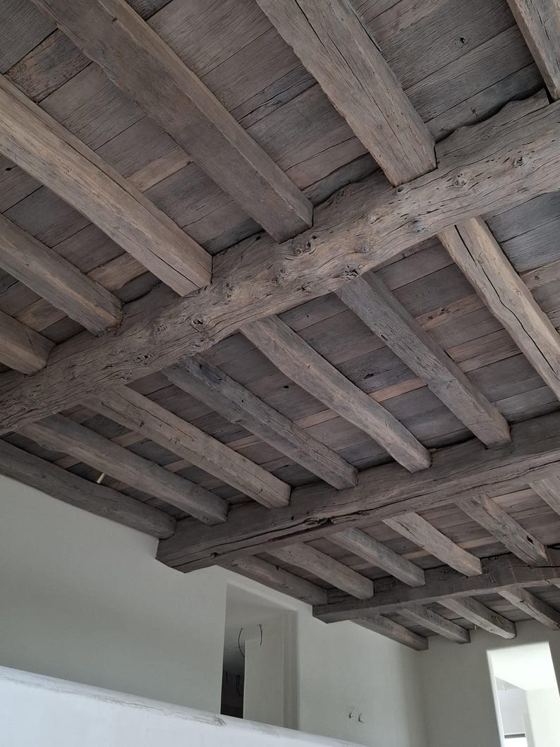 May include: A rustic wooden ceiling with exposed beams and planks. The wood has a weathered, gray-brown color, suggesting age and natural wear. The design features a grid-like pattern of beams and planks, creating a textured, architectural element.