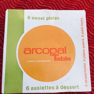 Könnte beinhalten: Eine weiße Schachtel mit grünem Rand und einem orangenen Kreis in der Mitte. Die Schachtel enthält 6 Dessertteller von Arcopal Table. Der Text auf der Schachtel lautet "6 sweet plates", "arcopal Table", "JG DURANT & Co 62510 ARDOES FRANCE", "6 assiettes à dessert", "6 dessertteller. 6 platos postre. 6 piatti frutta."
