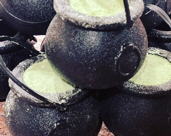 May include: A group of black cauldron-shaped containers with green powder inside. The cauldrons have handles and are stacked on top of each other.