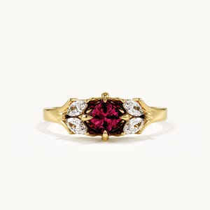 May include: A gold ring featuring a central square-cut deep pink gemstone held by four prongs, flanked on each side by two marquise-cut clear white stones set in a polished yellow gold band with a smooth, rounded finish.