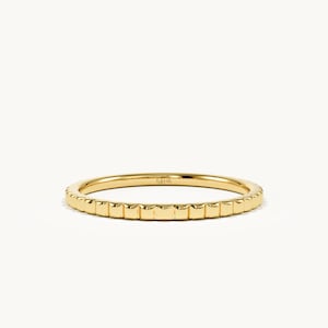 Può includere: Un sottile anello in oro giallo caratterizzato da un motivo testurizzato ripetitivo di piccoli segmenti rettangolari lungo l'intera fascia esterna. Il metallo ha una finitura lucida e riflettente, con l'interno marchiato 14K.