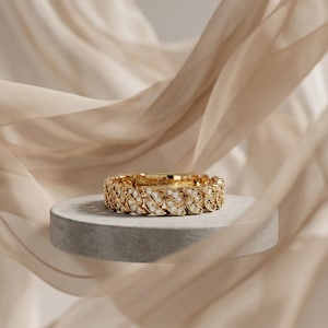 May include: A gold ring featuring a continuous chain-link design. The surface of the metal links is encrusted with small, clear, round-cut stones that reflect light. The band has a uniform width and a polished finish throughout its structure.
